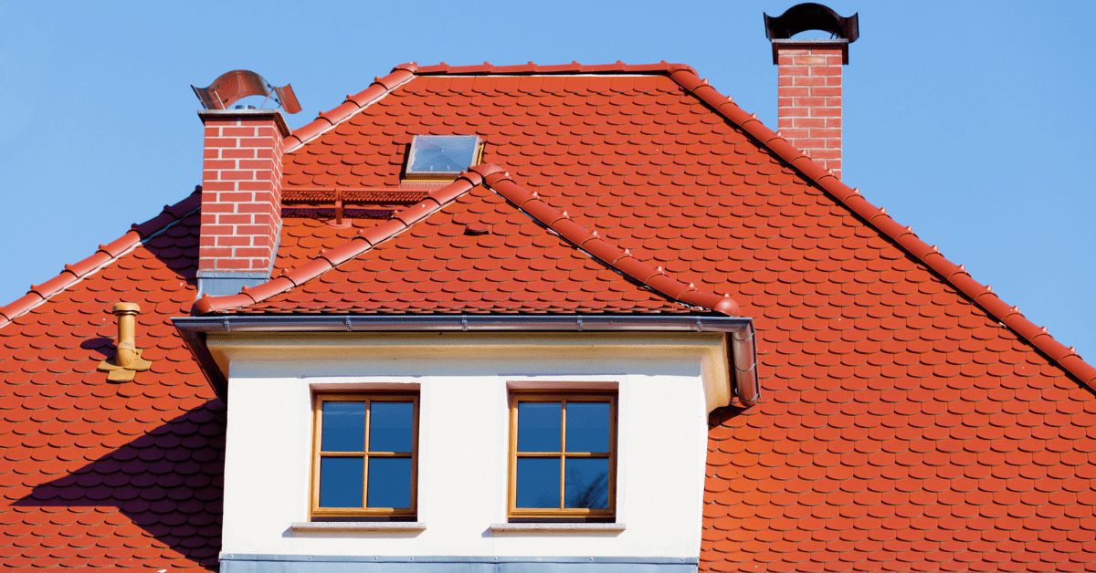 Red shingles on the roof of a white house with two brick chimneys